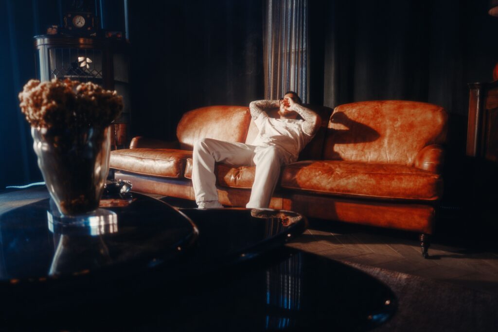 Um homem relaxa em um sofá de couro vintage em uma sala de estar preta aconchegante, cercado por uma iluminação ambiente quente. Psicologia do preto