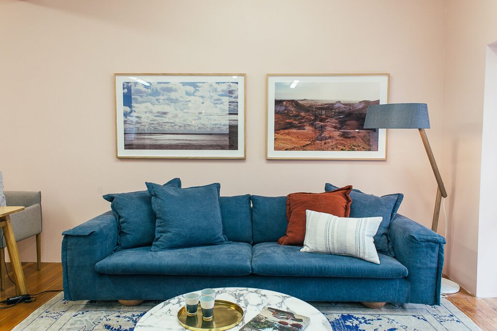 Um grande e confortável sofá azul com almofadas macias está posicionado em uma sala de estar moderna, com uma mesa redonda de mármore próxima à parede decorada com quadros. Psicologia do aZul