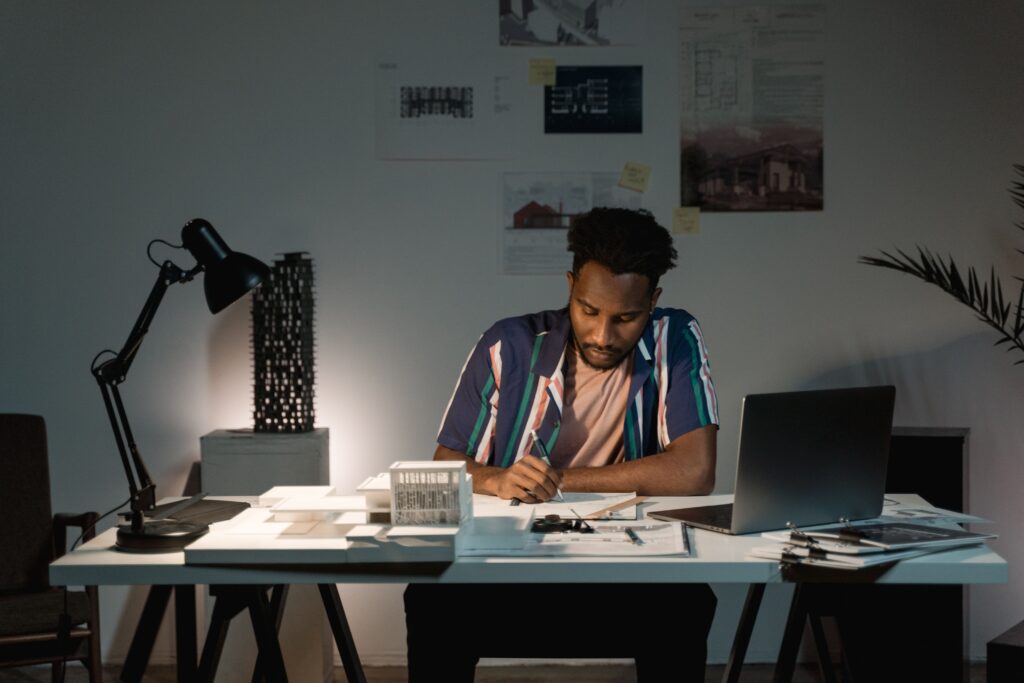 Um americano concentrado em sua mesa de escritório, em um ambiente pouco iluminado por uma iluminação para Home Office, cercado por documentos.