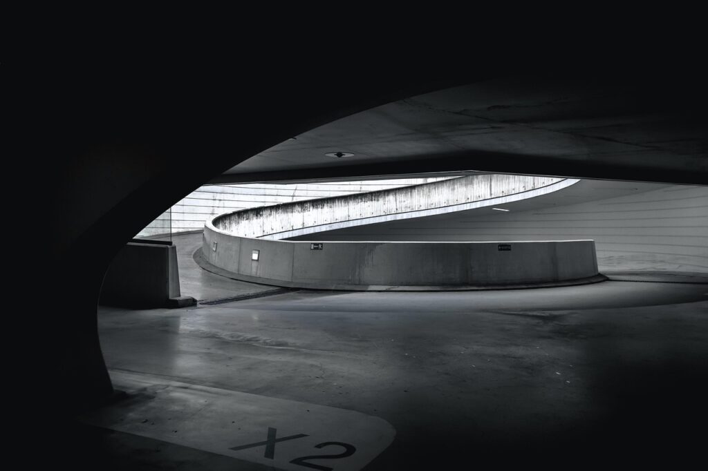 Perspectiva linear de um túnel estrutural de concreto cinza na Bélgica com iluminação embutida, demonstrando a psicologia do cinza através da solidez tectônica, da ordem geométrica e da condução do percurso visual.