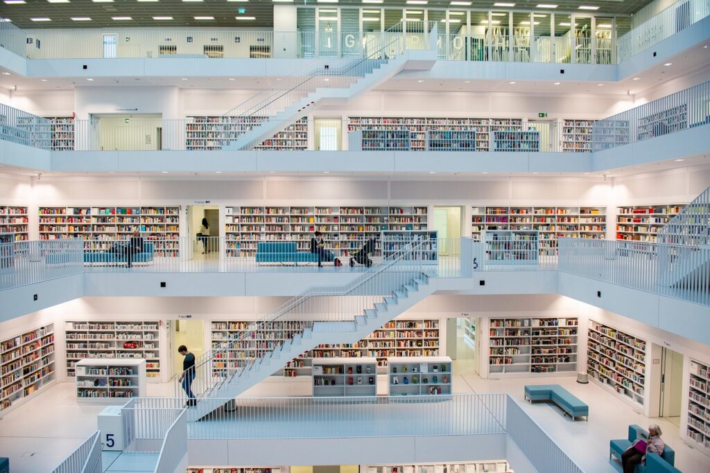 Interior de uma biblioteca contemporânea em Stuttgart com arquitetura moderna, onde escadas e estantes lineares de livros são emolduradas por superfícies alvas, evidenciando a psicologia do branco como um elemento de expansão espacial, ordem e neutralidade absoluta para o conhecimento.