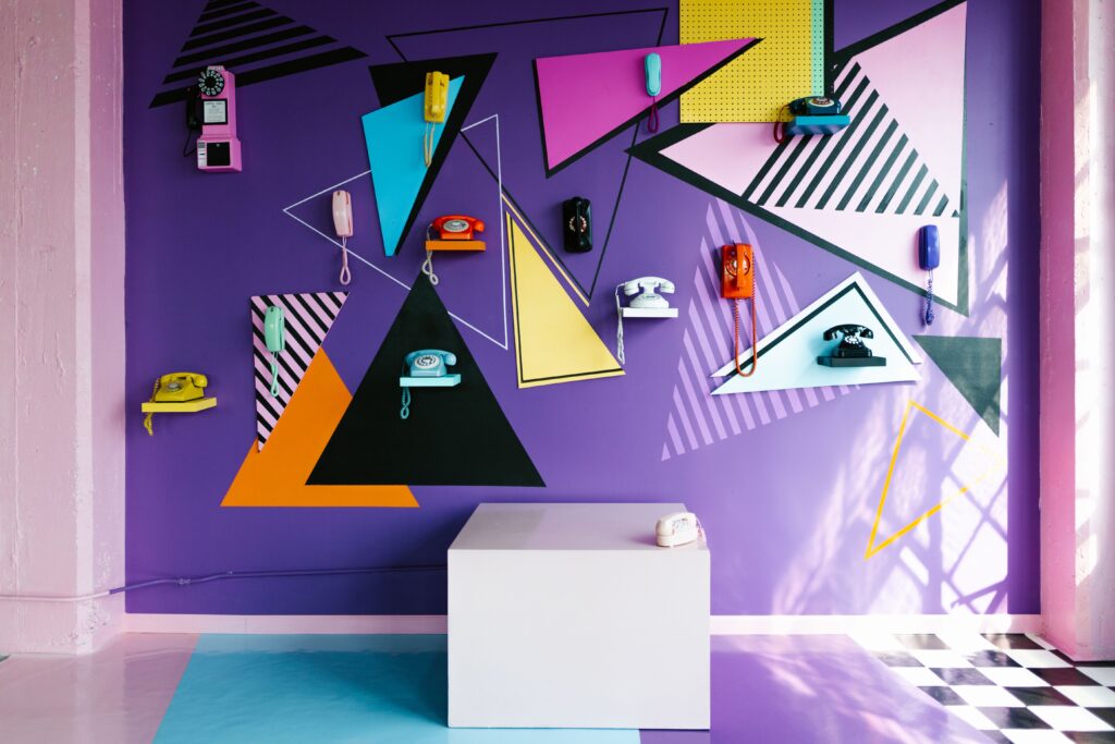 Exposição vibrante de telefones vintage em uma parede com padrões geométricos e tons de violeta, evidenciando a psicologia do roxo através de sua atmosfera lúdica, ambivalente e de estímulo à imaginação criativa.