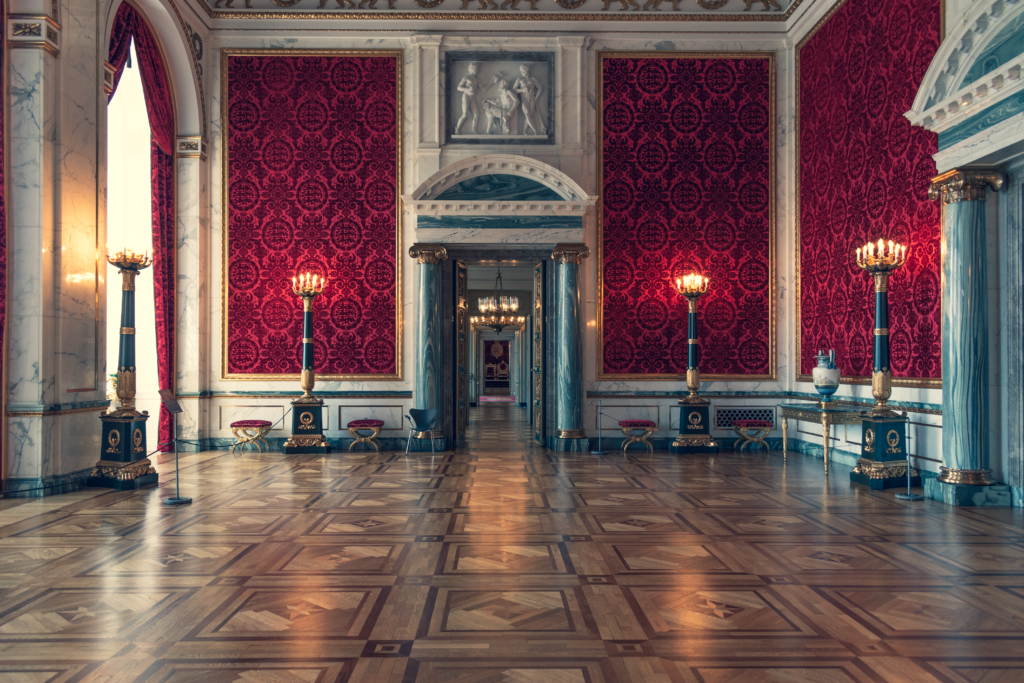 Interior luxuoso de uma sala de palácio com decoração vintage e detalhes ornamentados, onde tons profundos de vermelho evocam nobreza, elegância e introspecção dentro da psicologia das cores.