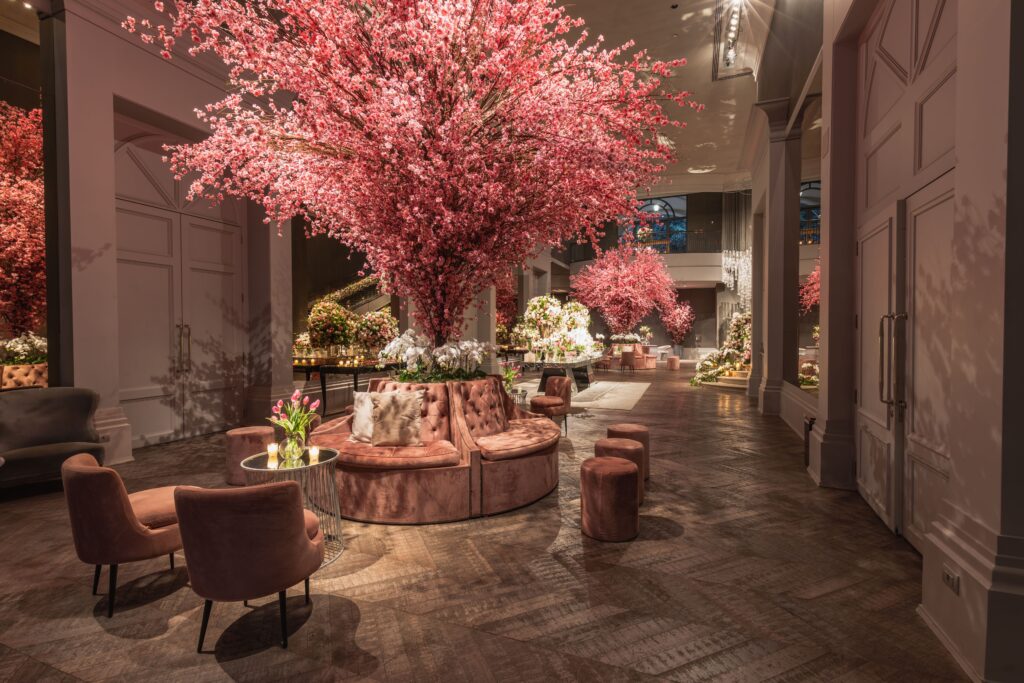 Lobby de hotel elegante apresentando arranjos de flores de cerejeira e assentos luxuosos sob iluminação quente, evidenciando a psicologia do rosa através do conforto visual, do desarmamento emocional e da criação de uma atmosfera de acolhimento sofisticado.