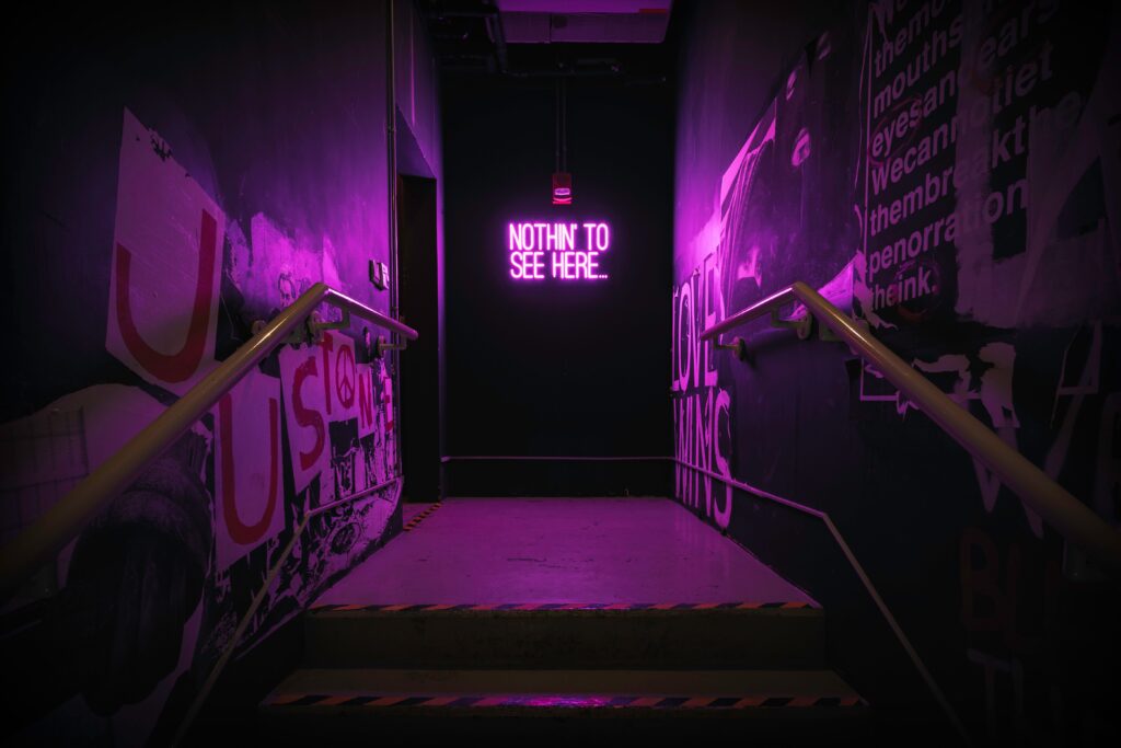 Escada dramática iluminada por neon roxo com um letreiro luminoso exclusivo criando uma atmosfera urbana, evidenciando a psicologia do roxo através do contraste cênico e da criação de uma identidade visual de exceção no espaço.