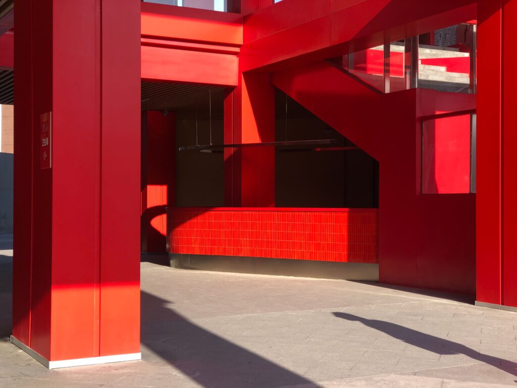 Arquitetura urbana contemporânea com tons ousados de vermelho e design geométrico projetando sombras dramáticas que evidenciam a psicologia do vermelho através do avanço visual e do contraste tectônico.