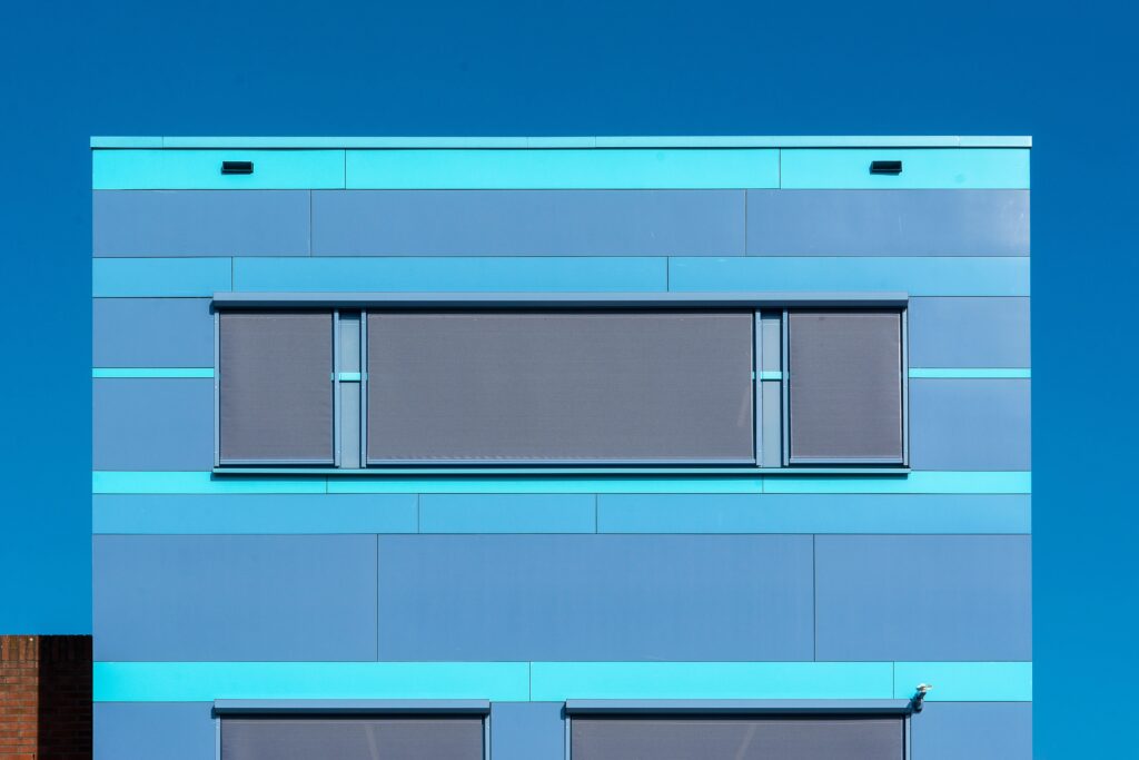 Vibrant blue modern building facade featuring sun shades against a clear sky.