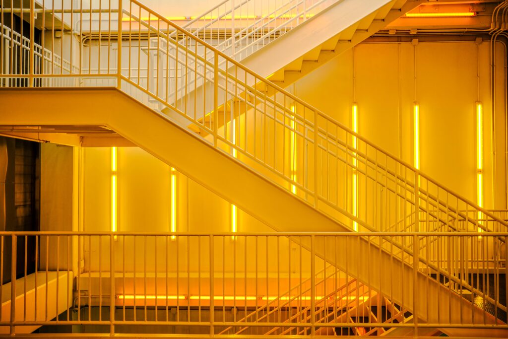 Uma escada contemporânea com luzes de neon amarelo brilhante criando uma atmosfera industrial, evidenciando a psicologia do amarelo como um estimulador mental imediato que quebra radicalmente a neutralidade do concreto.