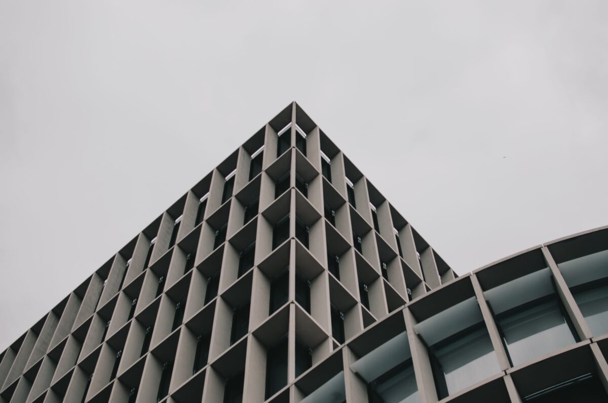 Vista em ângulo inferior de um edifício moderno com padrões de grelha geométrica contra um céu nublado, demonstrando a psicologia do cinza através de sua neutralidade absoluta e da capacidade de capturar micro-sombras sob a luz tropical.