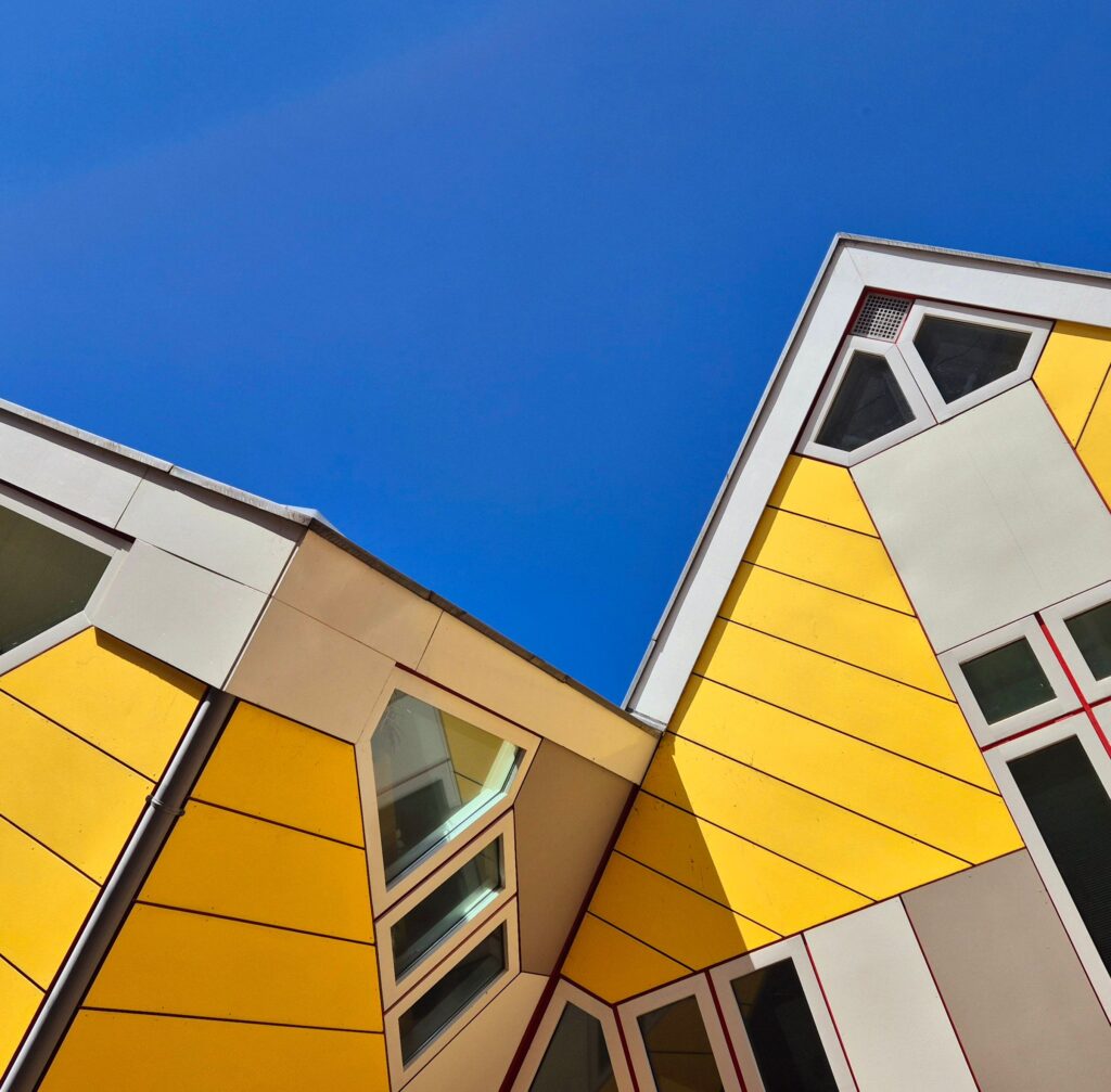 Arquitetura moderna e luminosa de casas cúbicas amarelas com design angular contra um céu azul claro, evidenciando a psicologia do amarelo por meio de seu caráter convergente, expansivo e de alta vibração cognitiva.