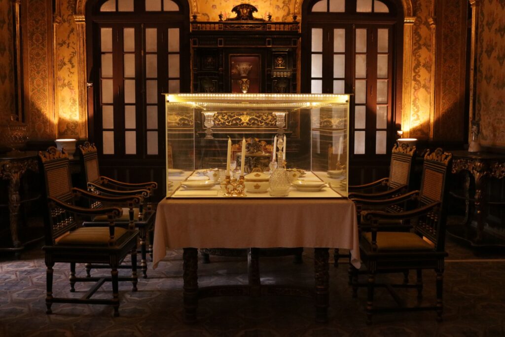 Elegante sala de jantar clássica apresentando móveis ornamentados e uma vitrine de vidro iluminada com louças, onde a psicologia do ouro atua através de eixos luminosos quentes para contrastar com a marcenaria escura e conferir nobreza ao espaço.