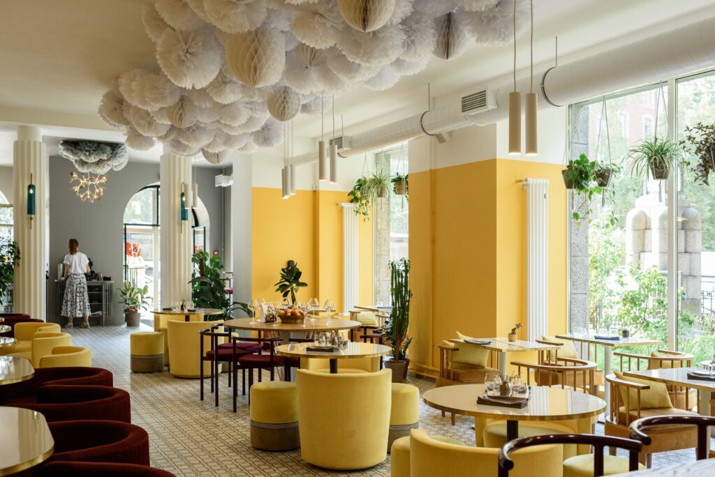 Design de interiores criativo de um café moderno e amplo com paredes e poltronas em amarelo brilhante, decorado com plantas verdes e luminárias aconchegantes, onde a psicologia do amarelo atua como um estimulador do intelecto, da comunicação e da troca social.