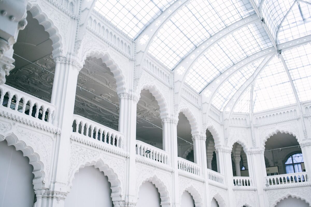 Ângulo inferior do Museu de Artes Aplicadas com paredes de pedra e varanda gradeada sob um teto brilhante na Hungria, demonstrando a psicologia do branco através do uso de superfícies alvas reflexivas para esculpir a luz e criar contraste tectônico com os elementos históricos.