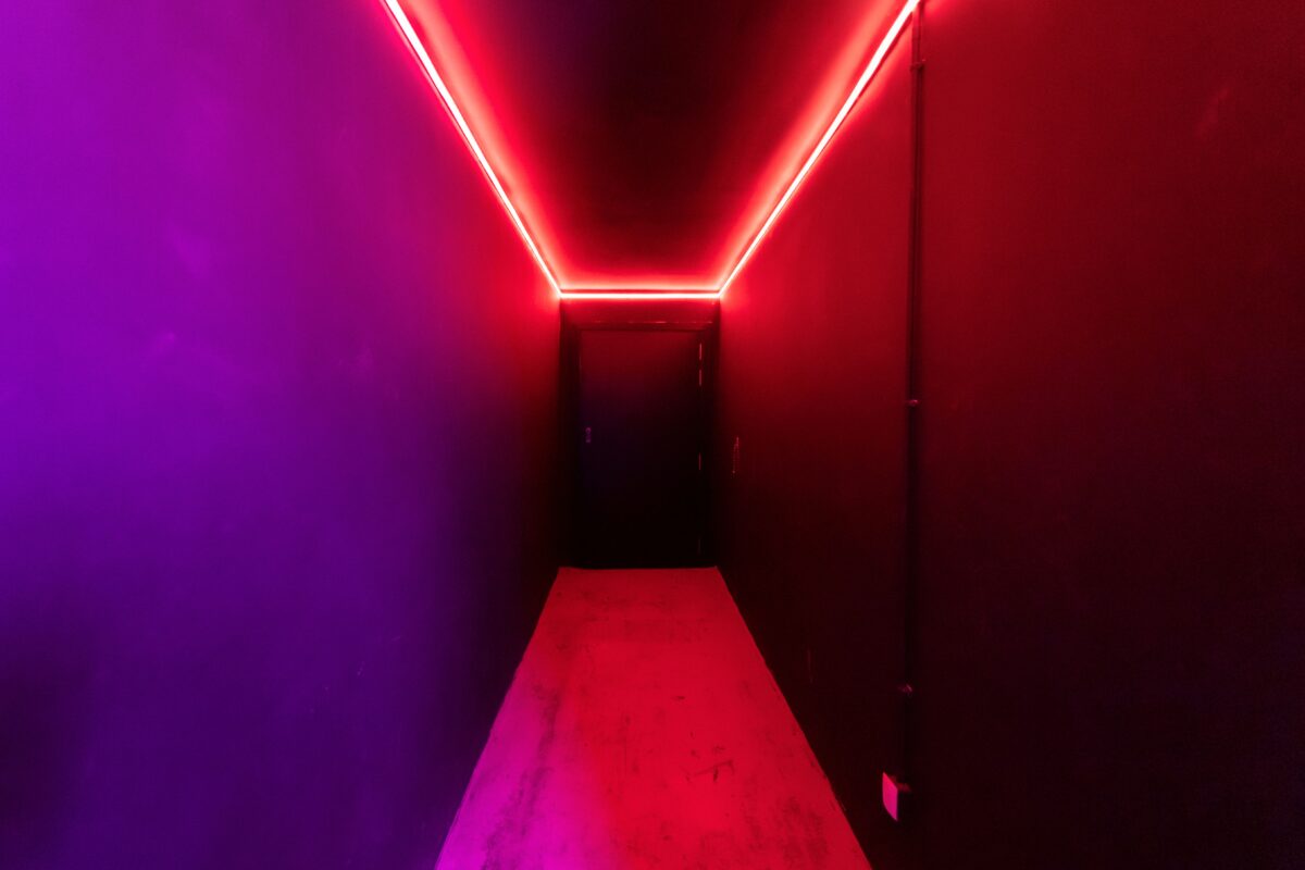 Um corredor vibrante iluminado por neon, apresentando uma mistura marcante de luzes vermelhas e roxas que evoca a psicologia do vermelho através do estímulo físico e da profundidade cênica.