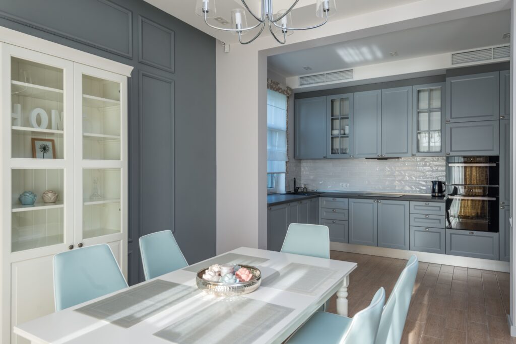 Interior de uma cozinha contemporânea com armários planejados em tom de cinza-azul francês e cadeiras de jantar em tons pastel, demonstrando a psicologia do cinza como um equalizador de contrastes que traz sofisticação e perenidade ao design.